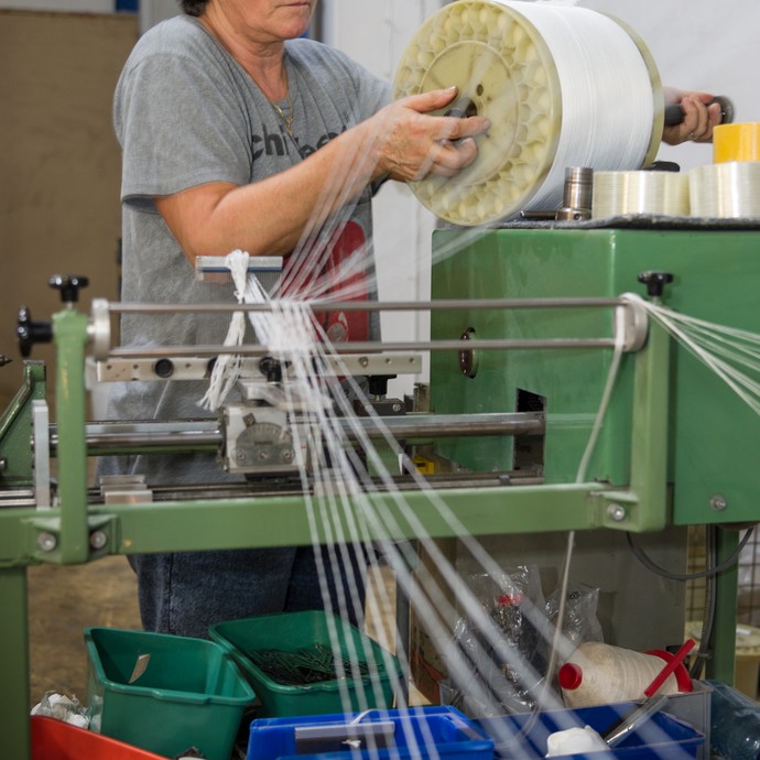 Maria da Silva hält eine Rolle mit Glasfasern in der Hand. Sie bereitet diese für den Webprozess vor. (vergrößerte Bildansicht wird geöffnet)